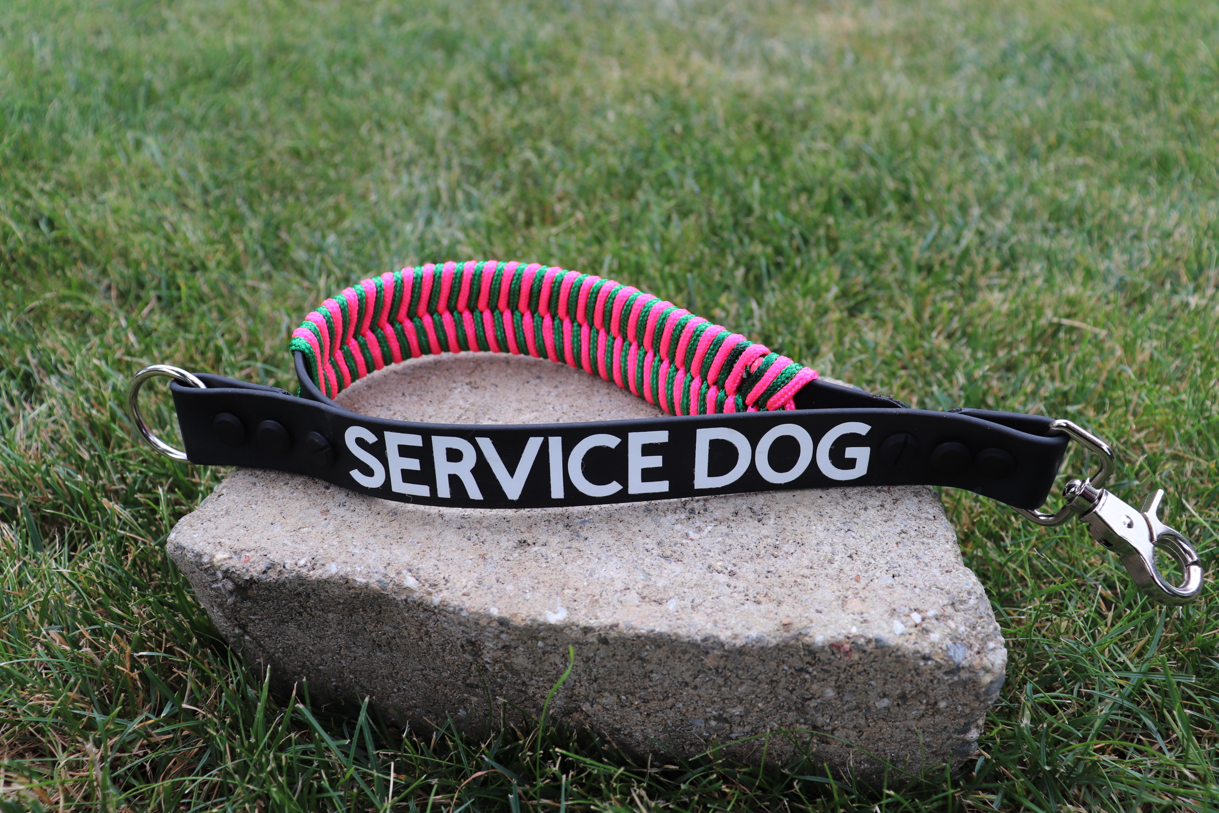 Item: Custom service-dog leash extender with built-in fishtail traffic handle | Width: 1 in | Colors: Black base with paracord fishtail in hot pink and green | Hardware: silver & black mix with special-order lobster-claw swivel snap | Custom: Mixed hardware colors, paracord fishtail traffic handle, and HTV phrase